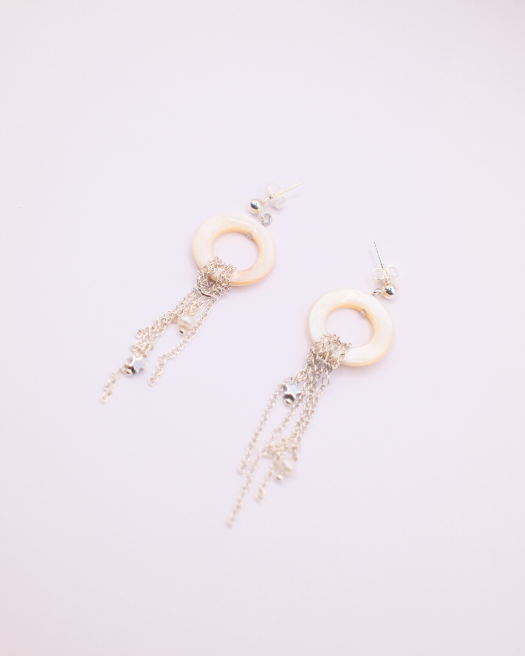 Statement earrings with white shell circle beads, strands of silver chain with star and pearl charms attached to silver studs.